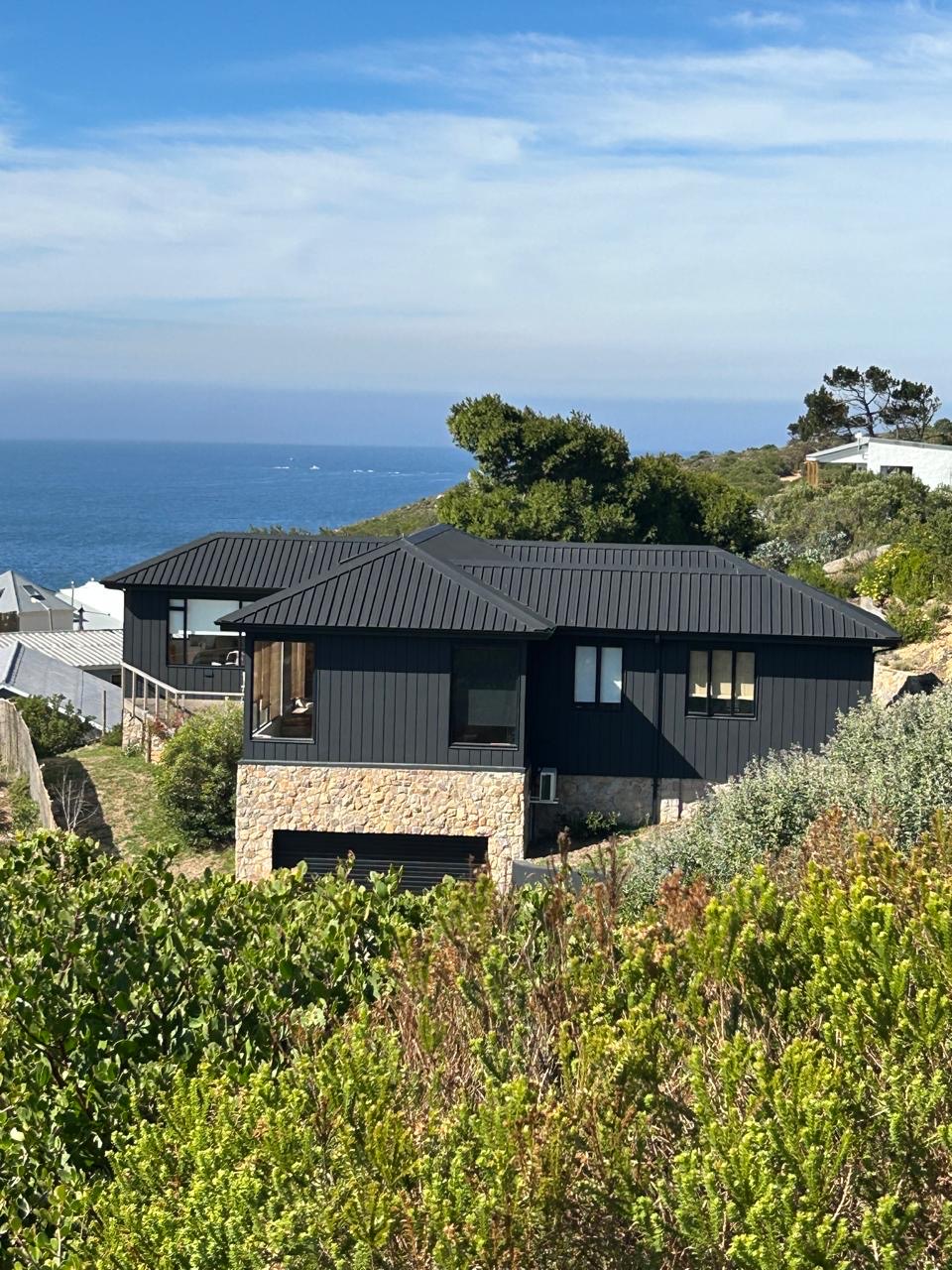 Completed home with dark cladding and stone-clad garage on a coastal hillside