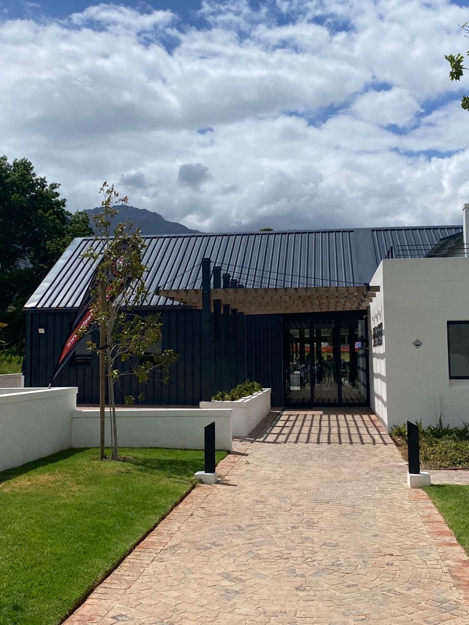 Finished building with dark steel cladding, white plastered walls and a timber pergola over the entrance