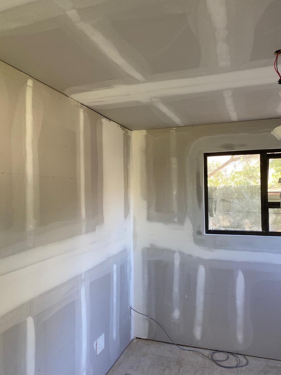 Interior room with drywall hung on walls and ceiling, joints taped and skimmed with compound but not yet painted