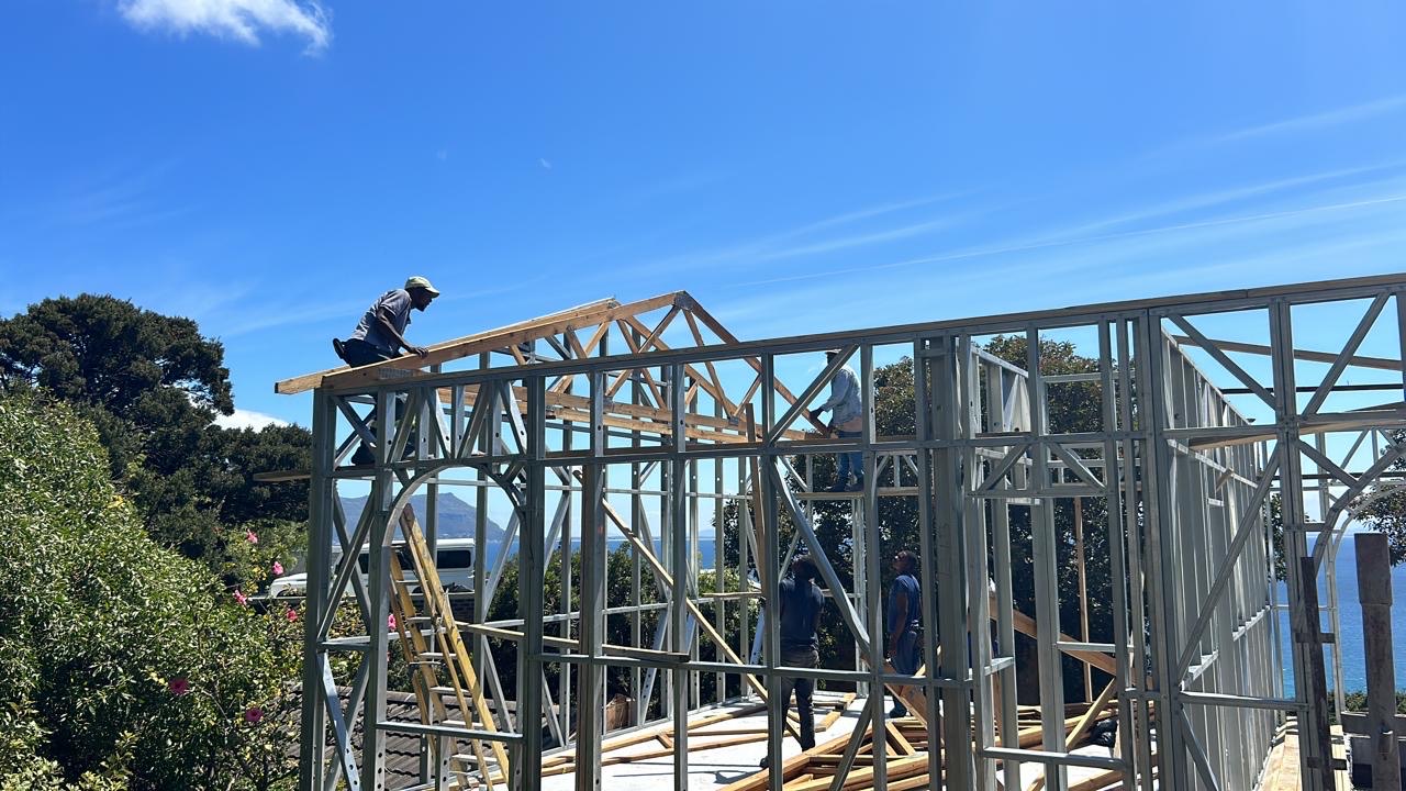 Crew lifting roof trusses onto a light steel frame on a coastal site