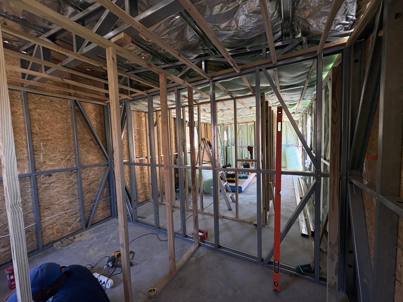 Inside an LSF build in progress: galvanized steel stud walls braced with timber posts, OSB sheathing on the outer walls, foil sarking and insulation batts in the roof